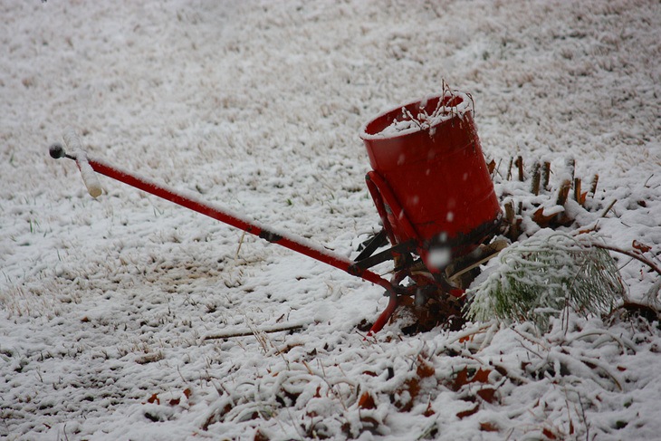 A red fertilizer spreader standing in the snow
