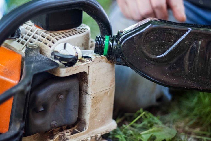 A lumberjack fills his gas-powered chainsaw with gasoline to continue working