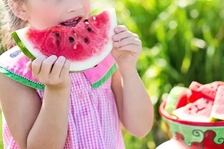 A little girl eating a watermelon with some seeds
