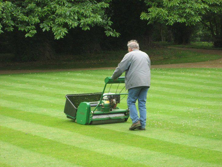 A man utilizing a lawn mower to keep the grass flat in his yard