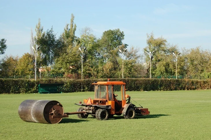 Tractor leveling soccer field grass using heavy metal lawn roller