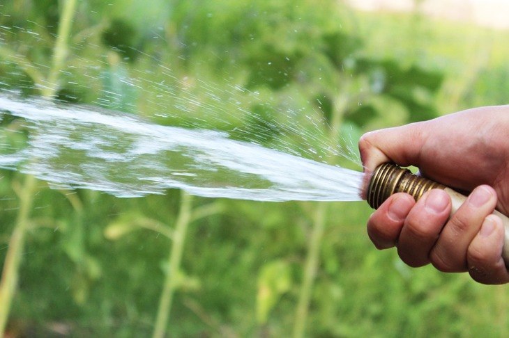 A man uses a garden hose for garden growth and soil compaction