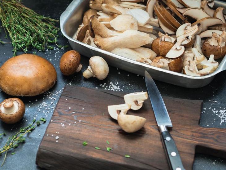 Raw Portobello Mushrooms on table with cutting board, knife, and herbs