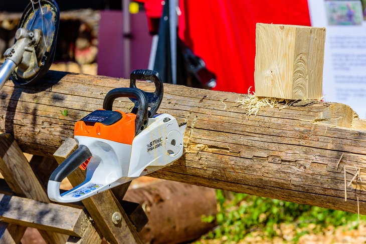 An electric-powered chainsaw lodged on lumber - Best Stihl Chainsaw For Cutting Firewood